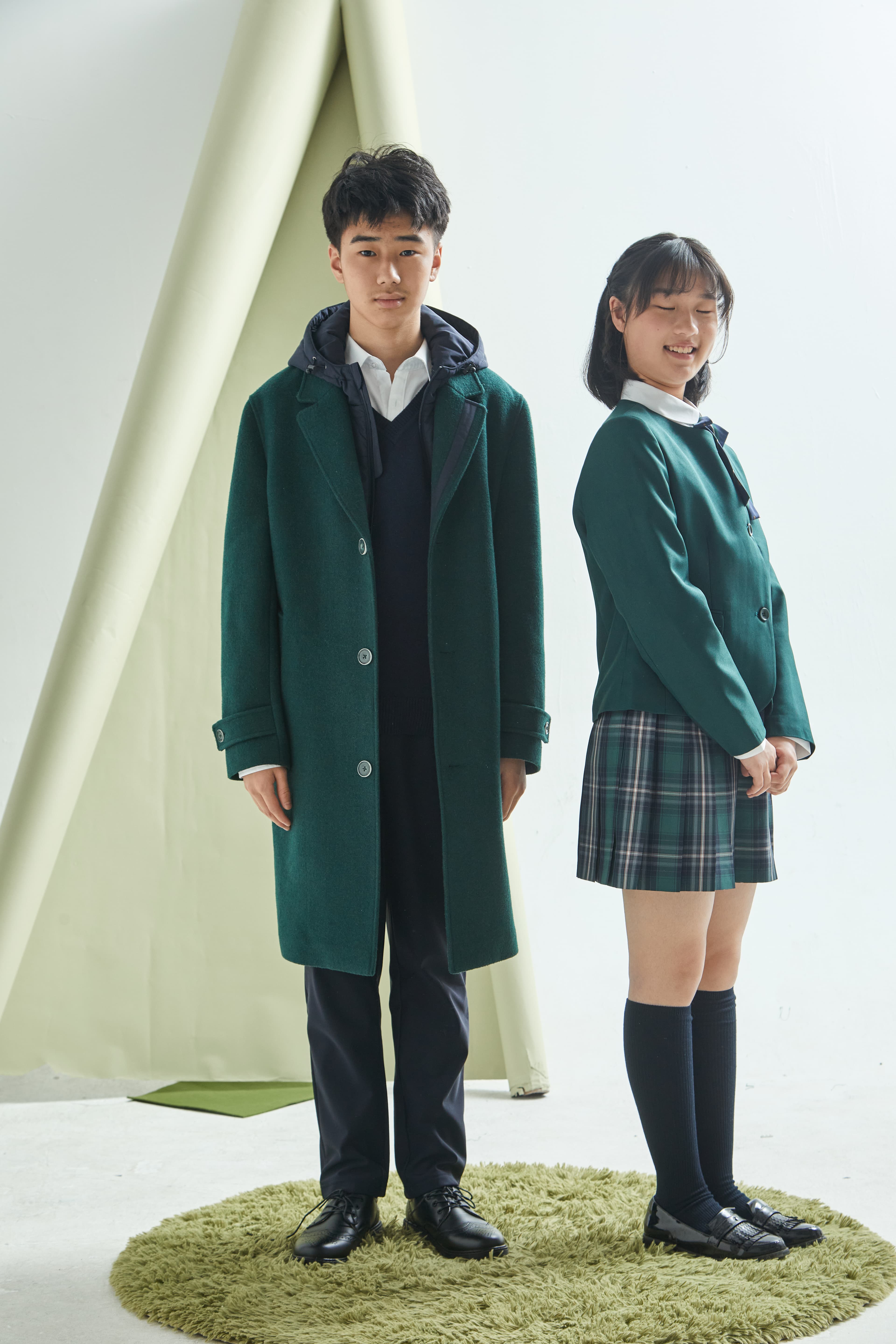 Boy and girl in green school uniforms pose on a green rug in a studio.