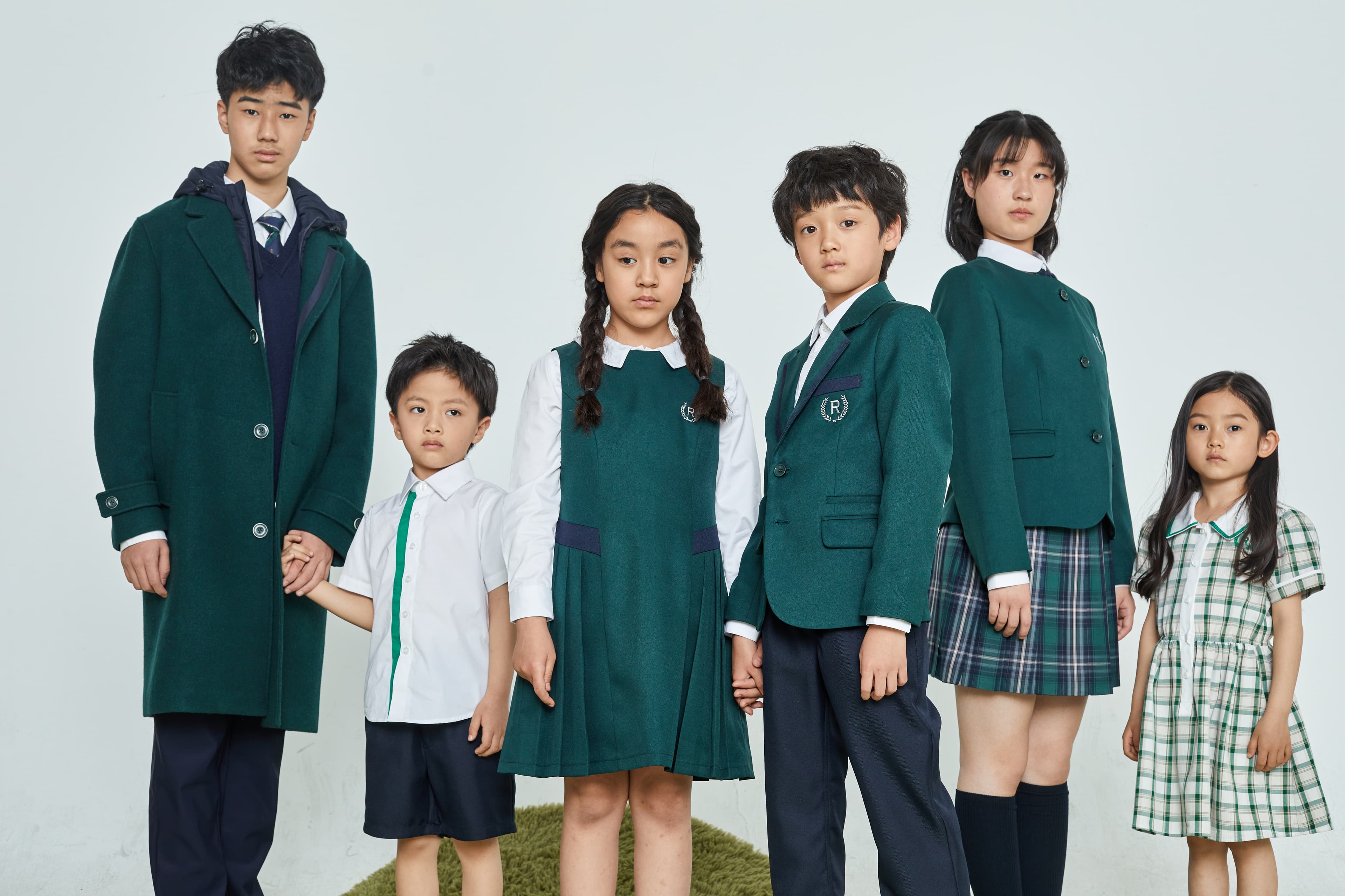 Six children of various ages wearing green and white school uniforms against a white background.