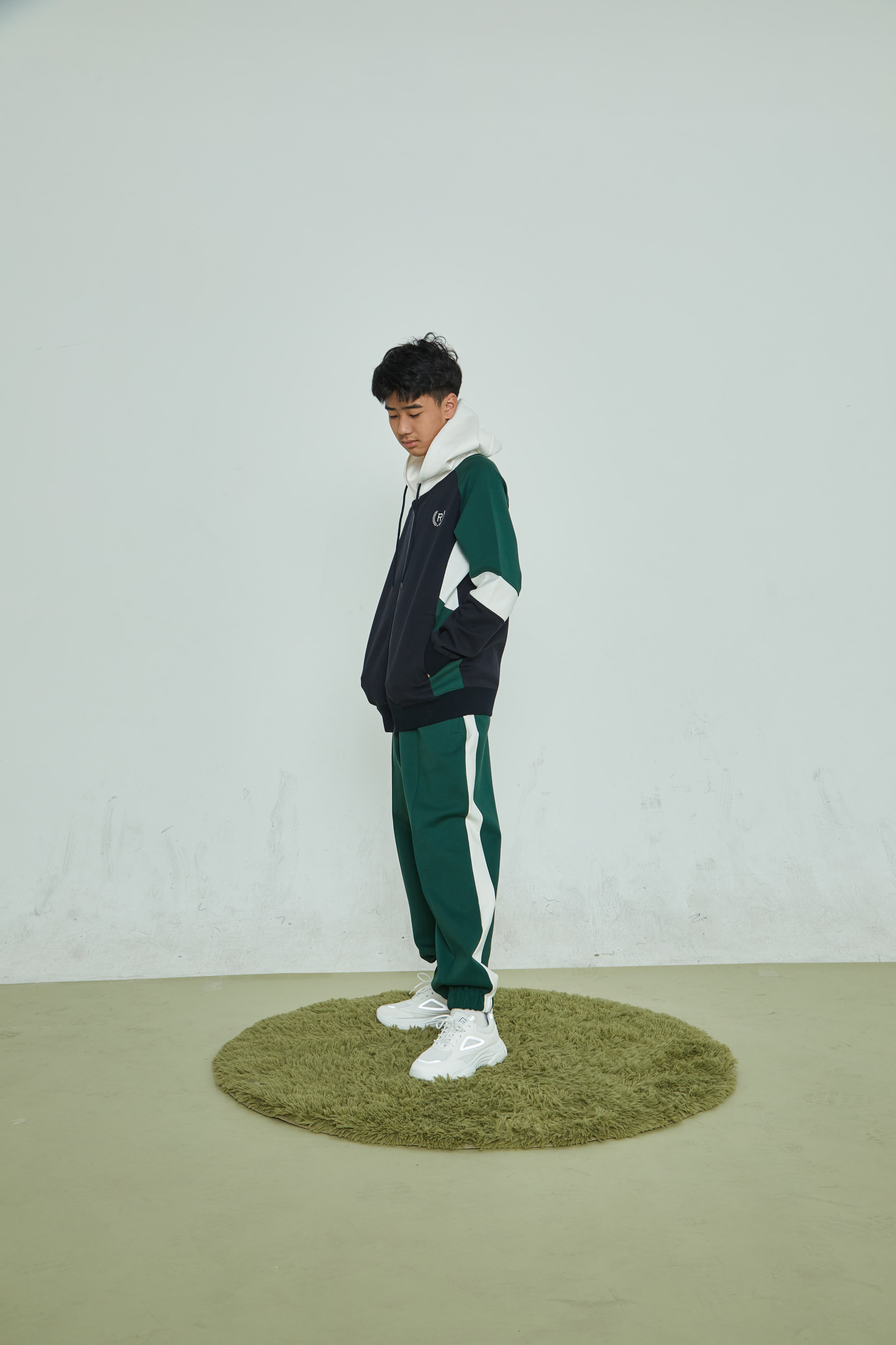 Young man wearing a green and navy color-blocked tracksuit on a small circular rug.
