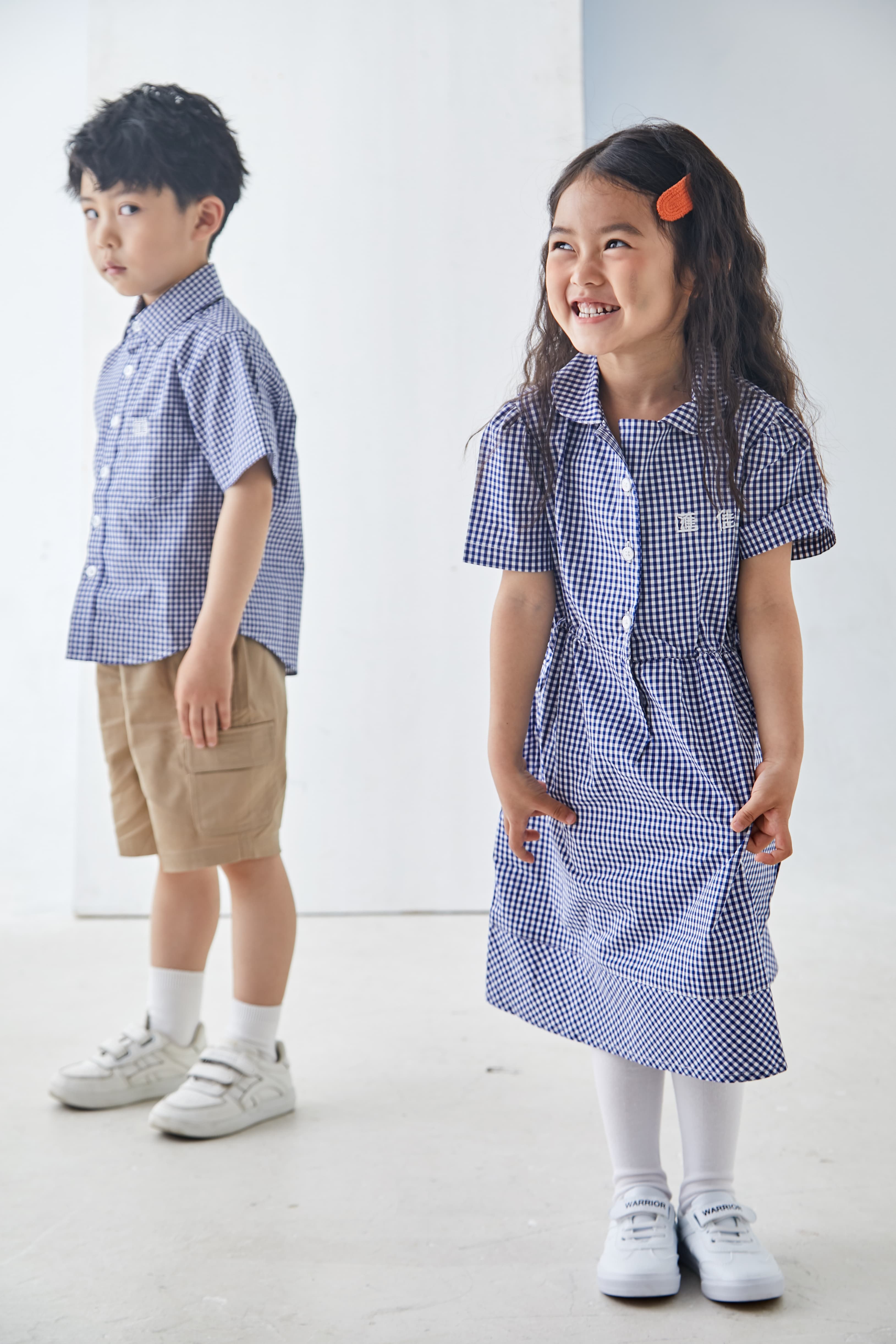 Smiling girl in blue gingham dress and boy in matching shirt against white background.